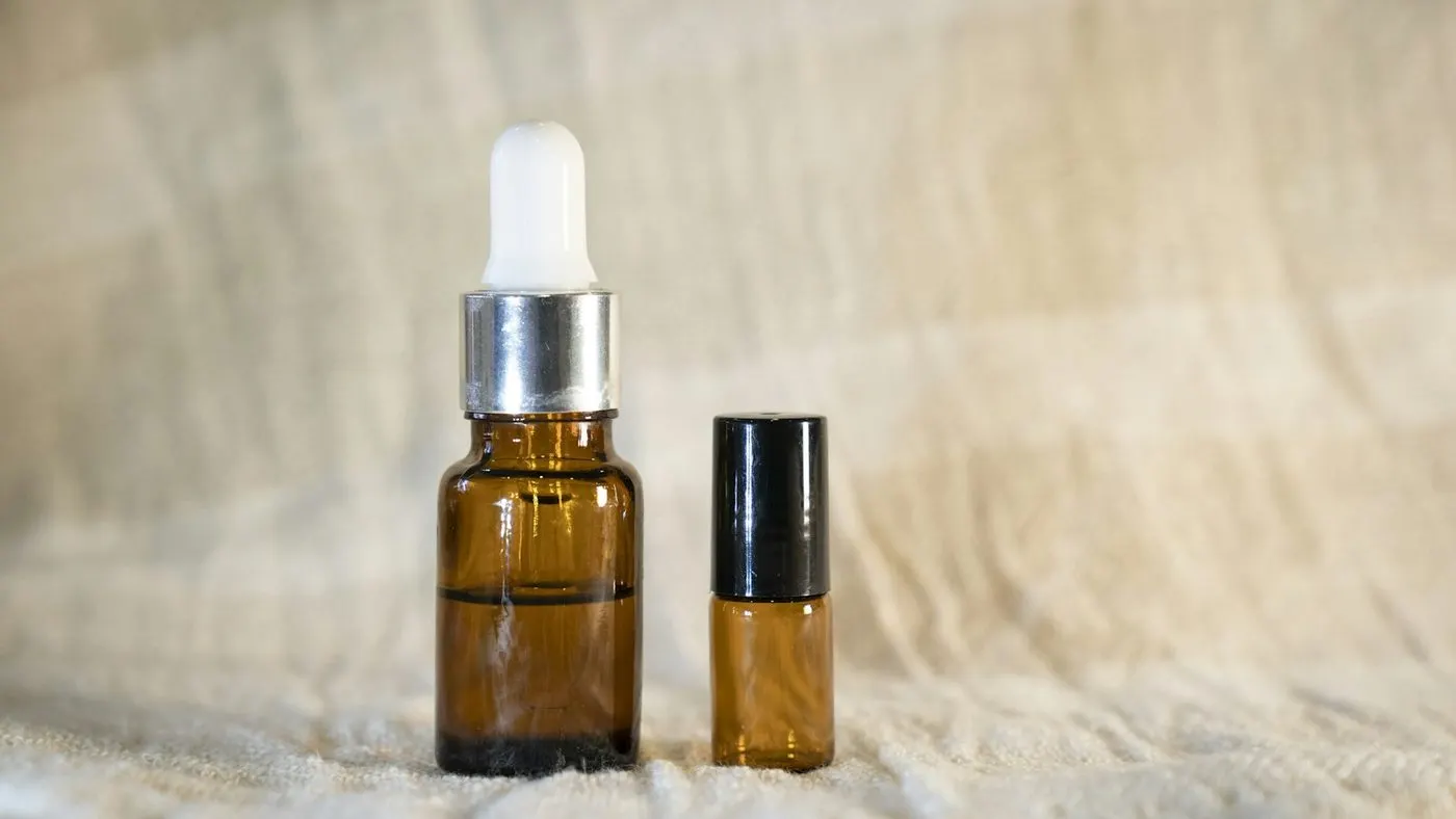 Two amber glass dropper bottles with pipette bulbs resting on a soft fabric surface.