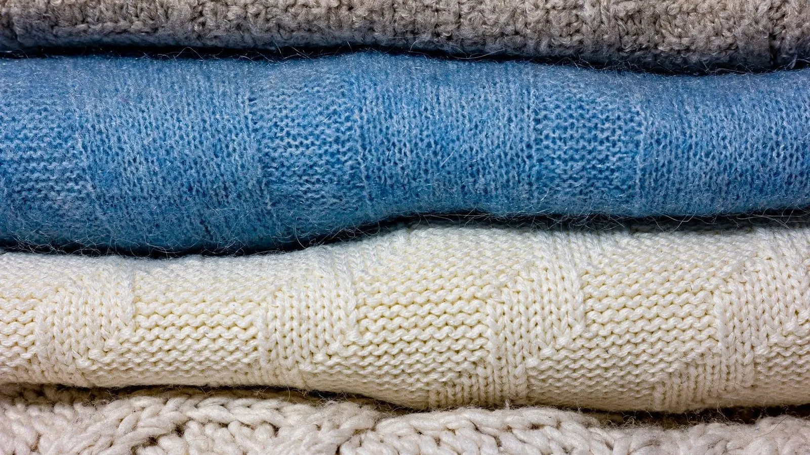 Stacked folded wool and cashmere knitwear, representing merino wool laundering and care.