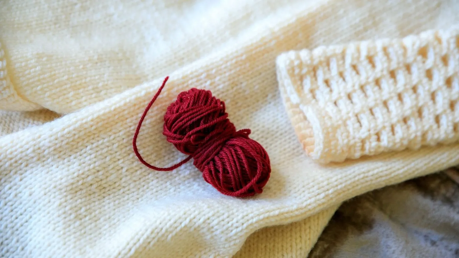 Cream knit with a ball of red yarn, representing cashmere spot treatment and wool care.