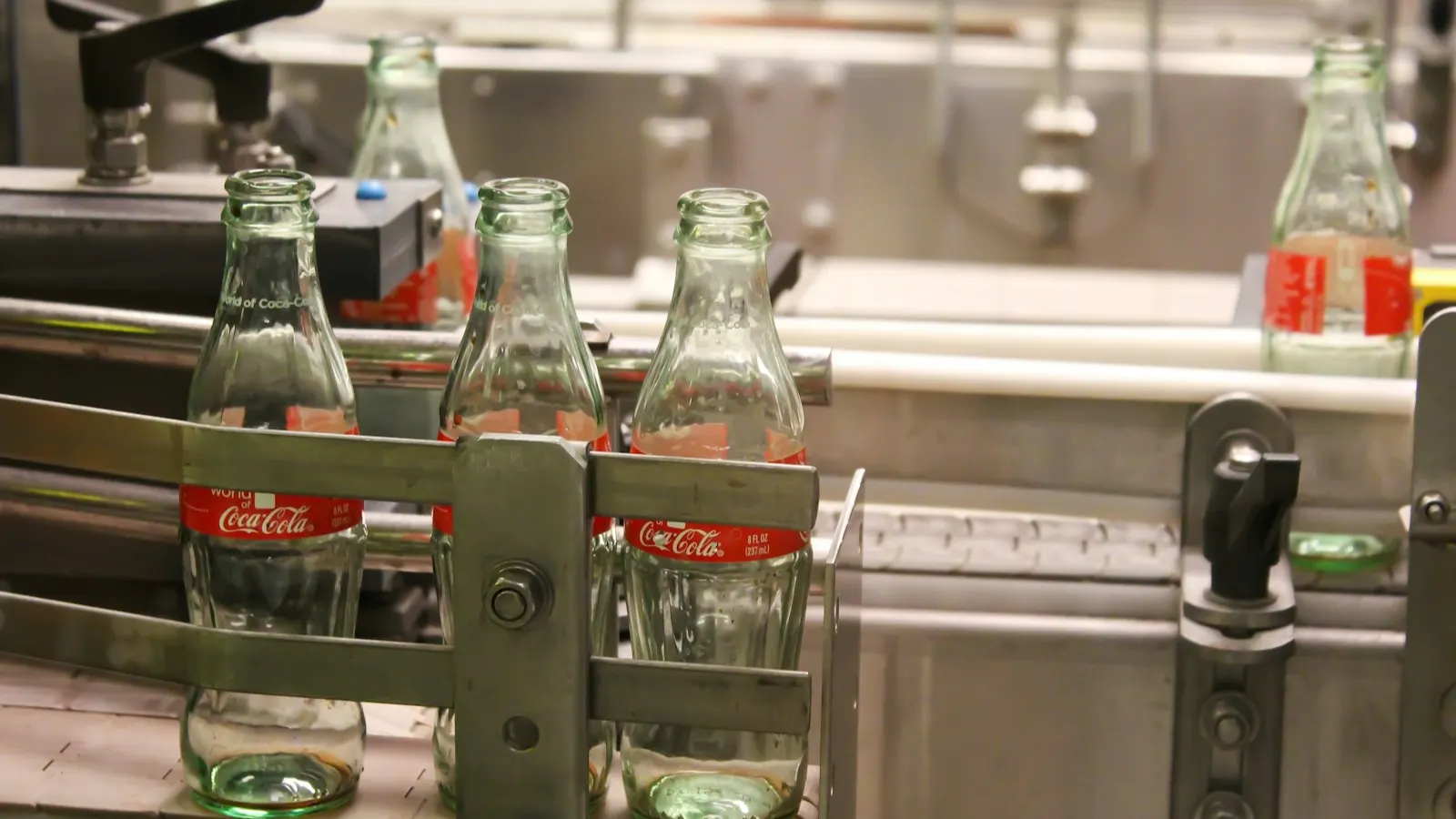 Bottles on a manufacturing line with printed label sleeves being applied, representing custom printed neck-band sourcing.